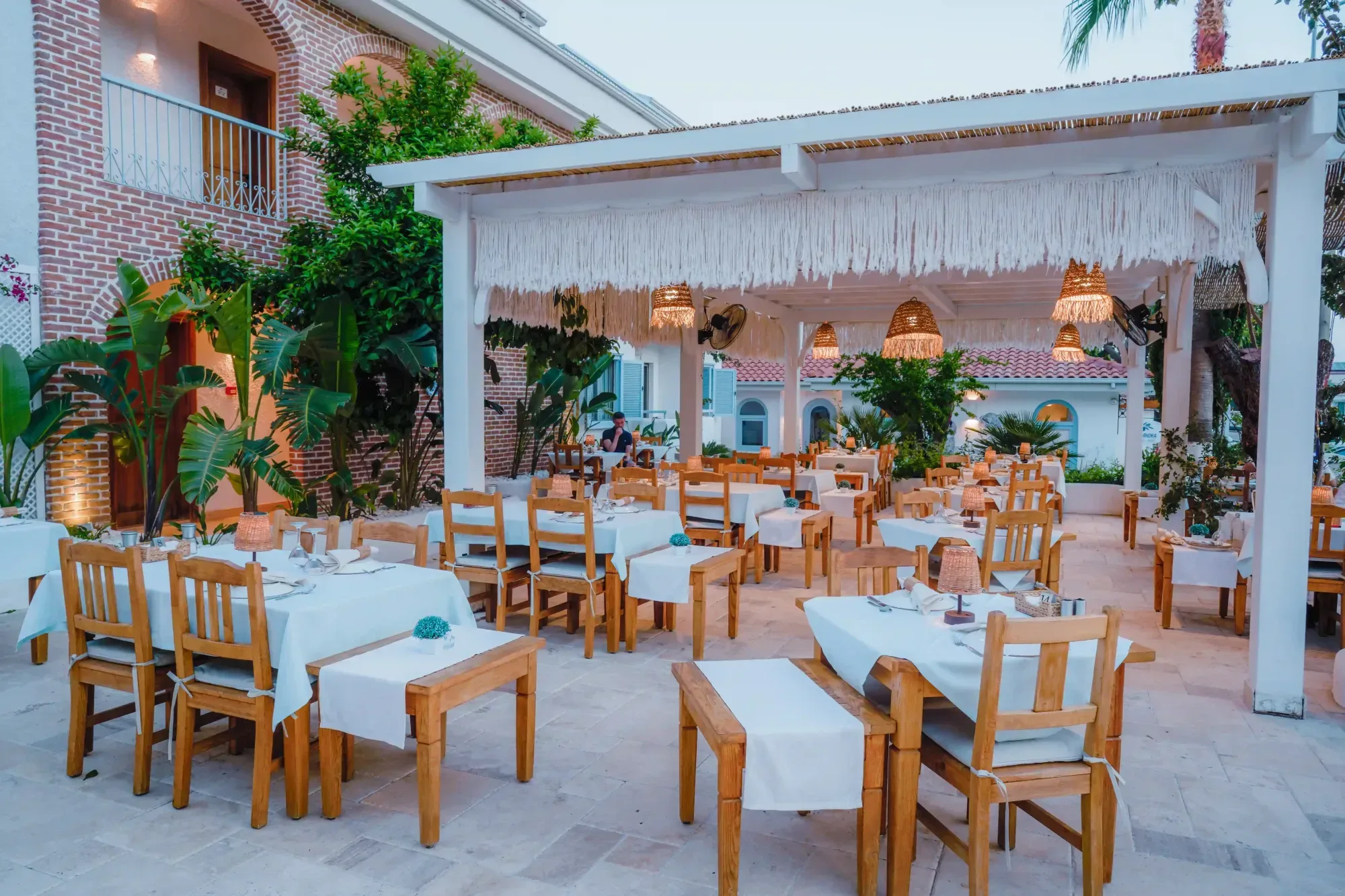 Ölüdeniz'de akşam yemeği için hazırlanmış Kassandra Restaurant dış mekan - pergola altında beyaz örtülü masalar